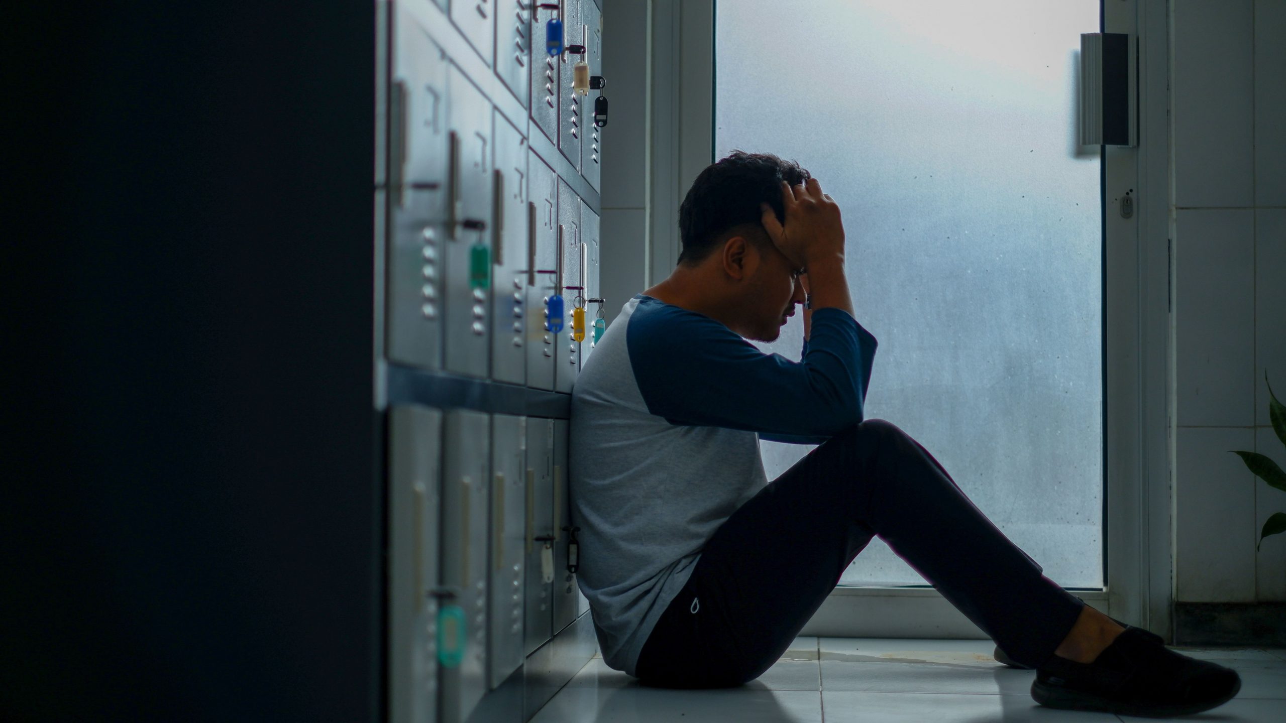 "Depressed teenage boy sitting next to a locker feeling overwhelmed"